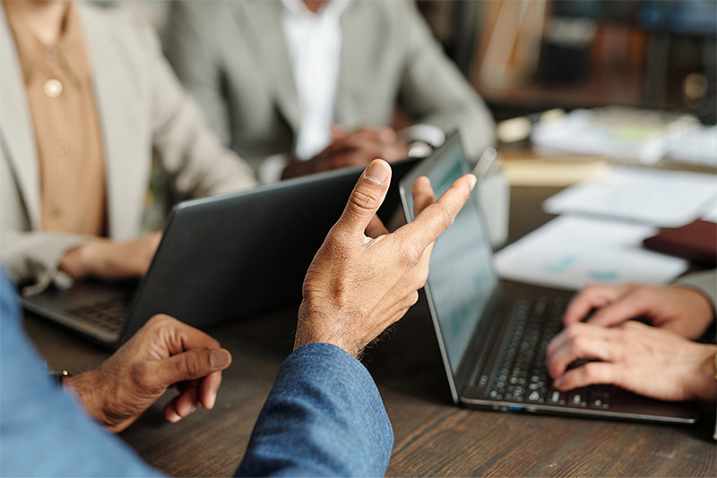 Close-up of a meeting with people using laptops, one person gesturing while speaking