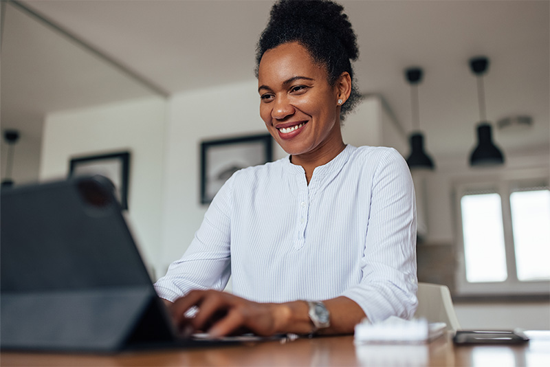 Woman smiling and typing on a laptop while seated at table