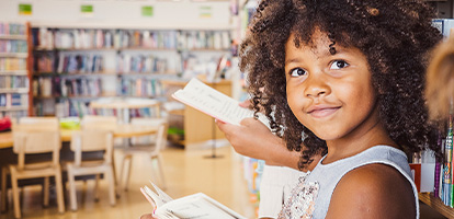 Elementary school children in a library leaning against a wall of books and reading