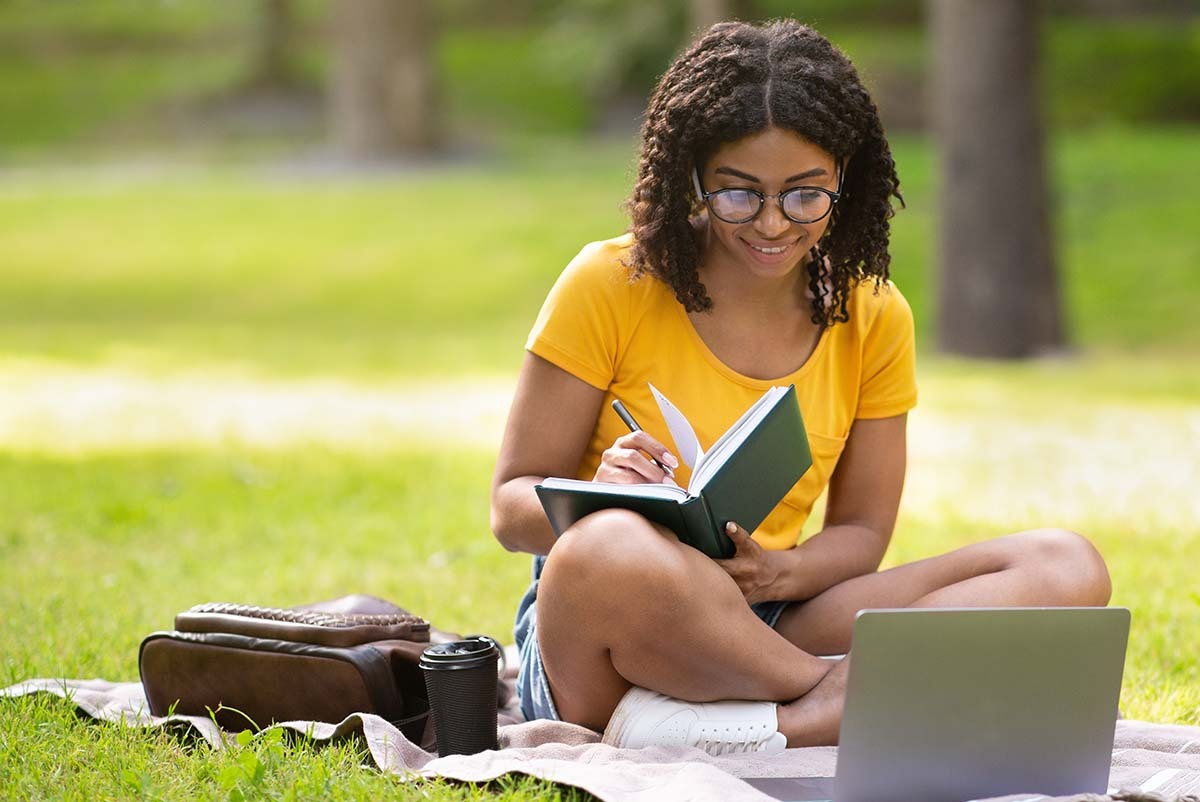 High schooler sitting on the grass reading a book.