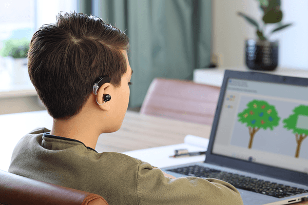 Student with a hearing aid learning on a laptop.
